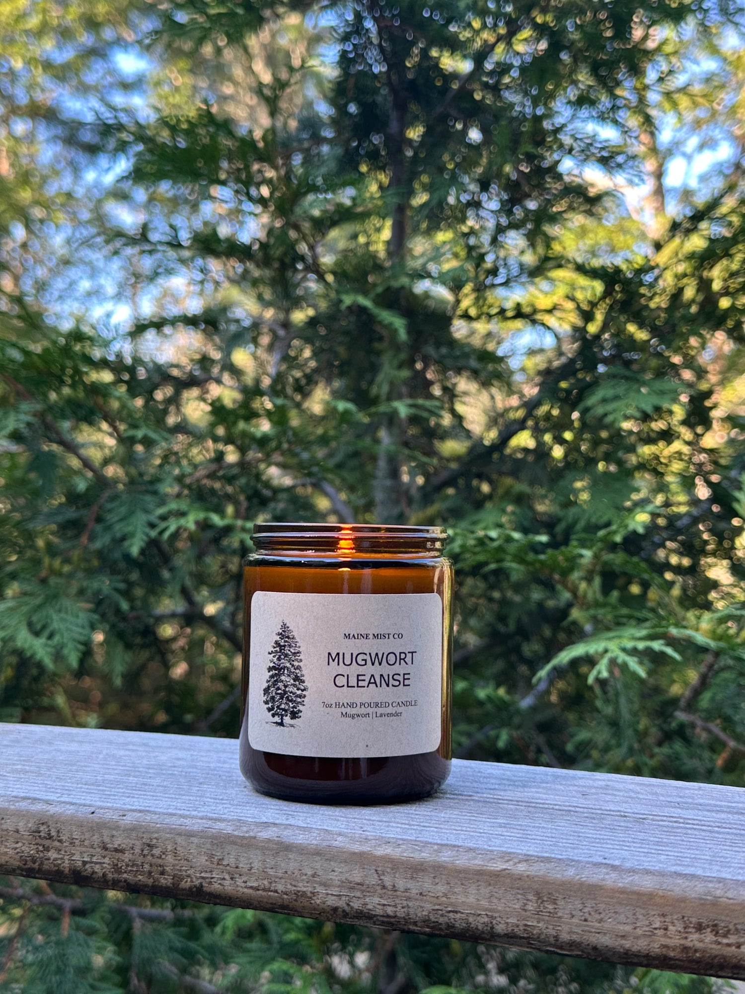 Amber candle in jar with a label on a wooden surface with trees in the background